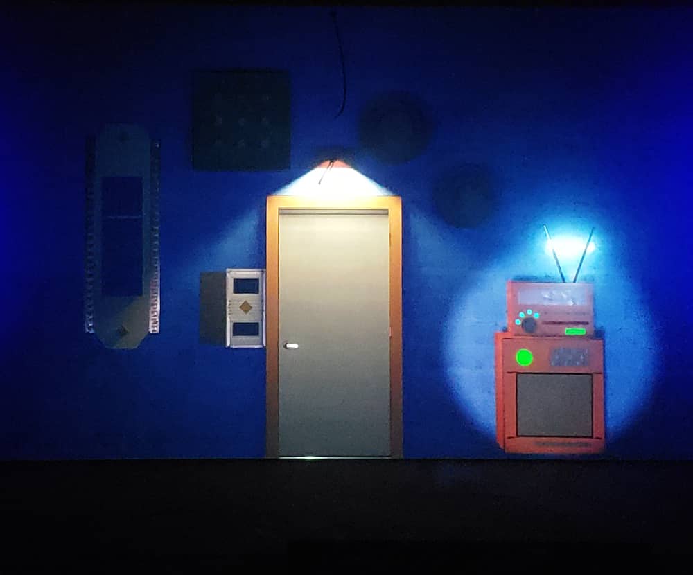 Projection of an escape room like environment. Includes a door and a mysterious technological contraption.