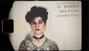 Mugshot of suspect 1, Ms Dockett. A well-dressed, professional woman with an intense gaze.