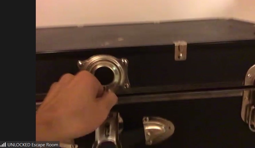 Hands opening a locked trunk viewed through Zoom.