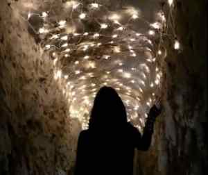 A woman in black walking through a dramatically lit cave.