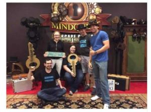 three men and 2 women are posing with giant prop keys in an escape room lobby