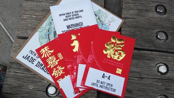 Some papers on a park bench, with several red envelopes, the top one of which reads "Do Not Open Until Instructed!"