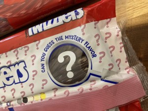 A magnifying glass with a question mark, surrounded by the text, "can you guess the mystery flavor"
