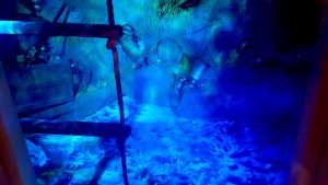 Porthole view of the bottom of the sea, assorted treasures lay about the sand.