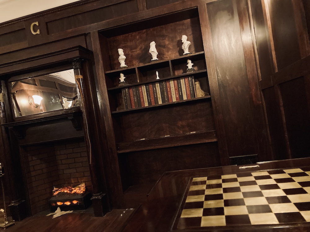 In-room: a bookshelf, fireplace, and chess board in a study.