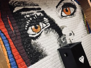 A massive mural of a woman's eyes painted on a brick wall. Below it is a display case for a diamond.