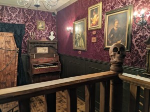 A skull on a railing in an ornate room with portraits hung on purple walls.