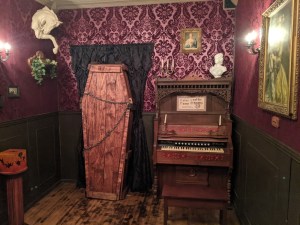 A coffin beside an organ in a very dramatic and ornate purple room.