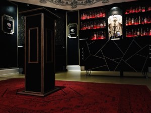 A beautiful black, red, and white magician's bar. Behind the bar are many bottles and a straightjacket worn by Houdini.
