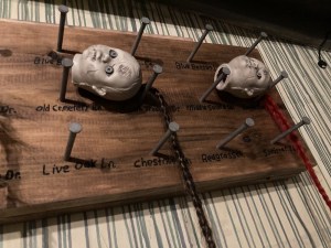 A wooden plank with many nails attaching dead looking doll heads.