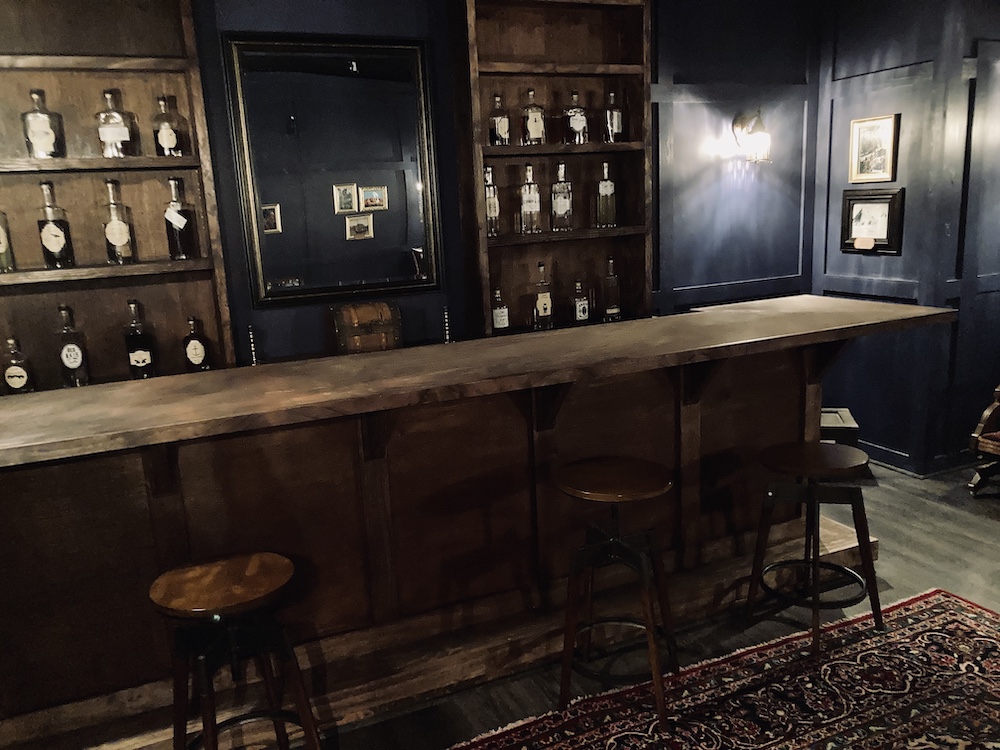 A large wooden bar with an assortment of bottles on the shelf beyond it.