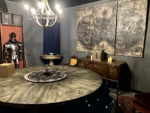 A large, circular wooden table surrounded by a large map and a suit of armor.