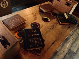A few piles of magical books on a wooden table twi colorful circles atop it.
