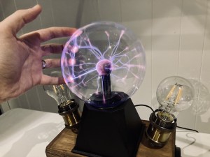 A hand reaching out towards the Tesla Box, and reaching for the glowing electron ball.