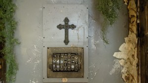 A large cross on a plaster wall, below it is a set of dials with different symbols.