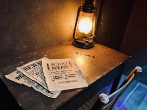 A small wooden table with a lantern, a pen, and a few wanted posters.