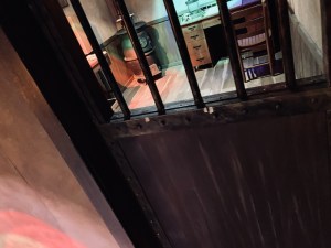 A barred jail door, the sherif's office is visible beyond the bars.