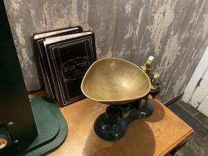 Closeup of a metal balance beside some Hebrew books.