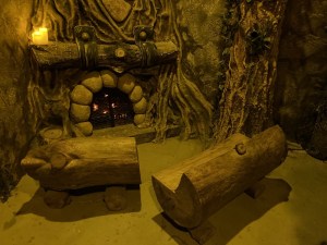 Interior of a fairy house, with small wood benches and a fireplace.