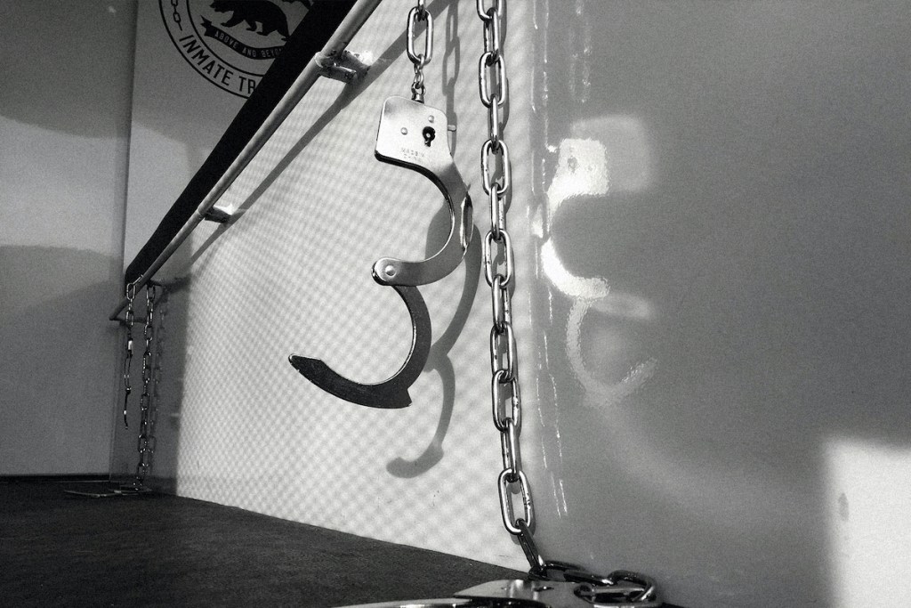 Unlocked handcuffs hanging from a metal bar.