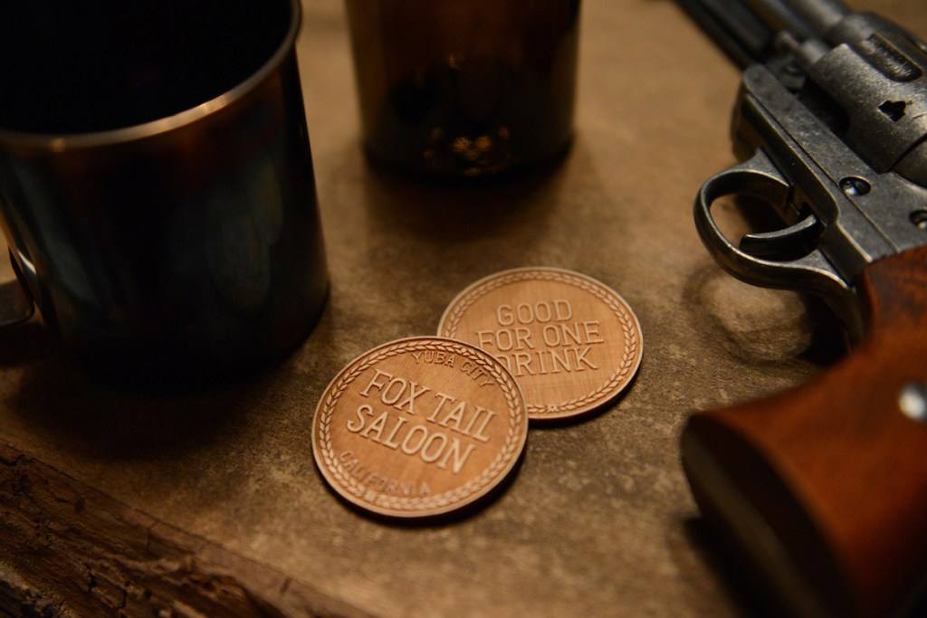 Closeup of two drink coins for the Fox Tail Saloon beside a 6 shooter.