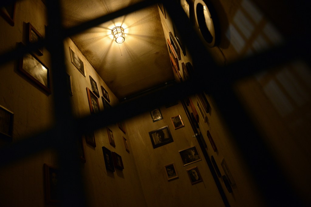 View through a cage door of a room covered in framed photos.