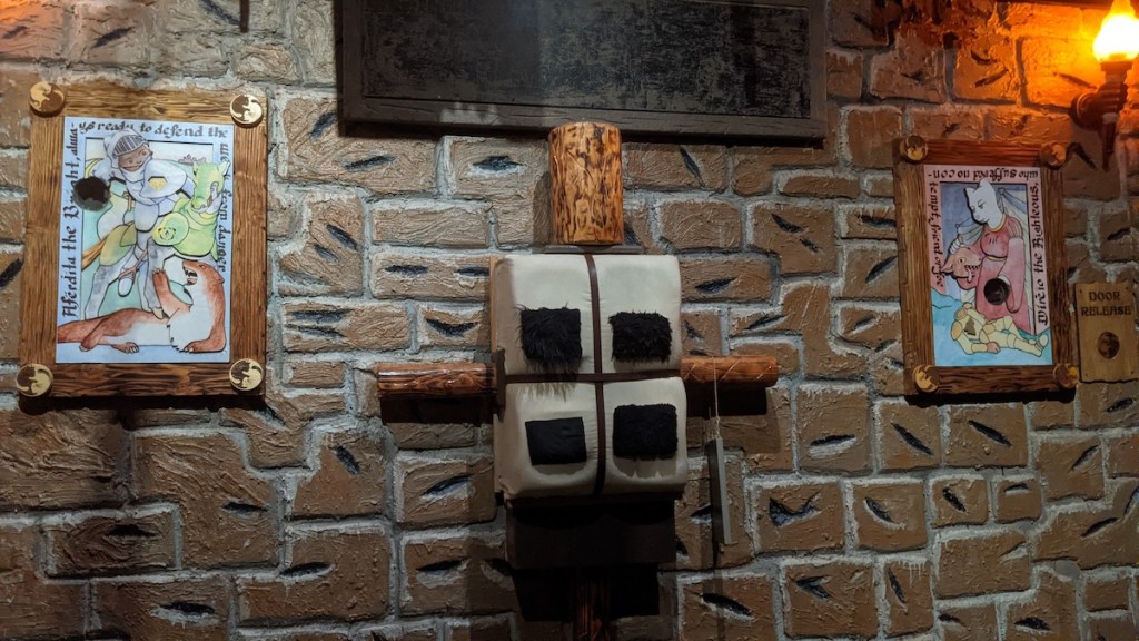 An unusual device mounted to the wall between two paintings of cats.