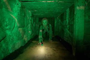 A woman crawling in a tunnel looking scared.