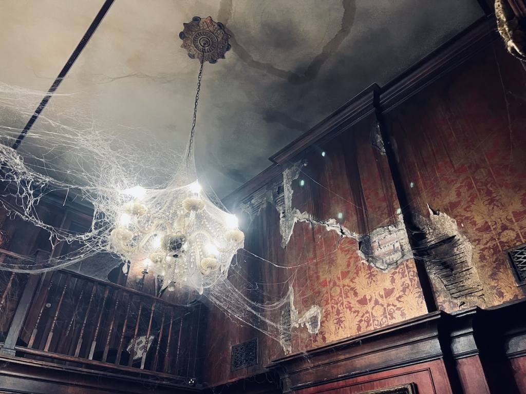 The ceiling and walls of a haunted house. It's covered incobwebs, and damaged plaster walls.