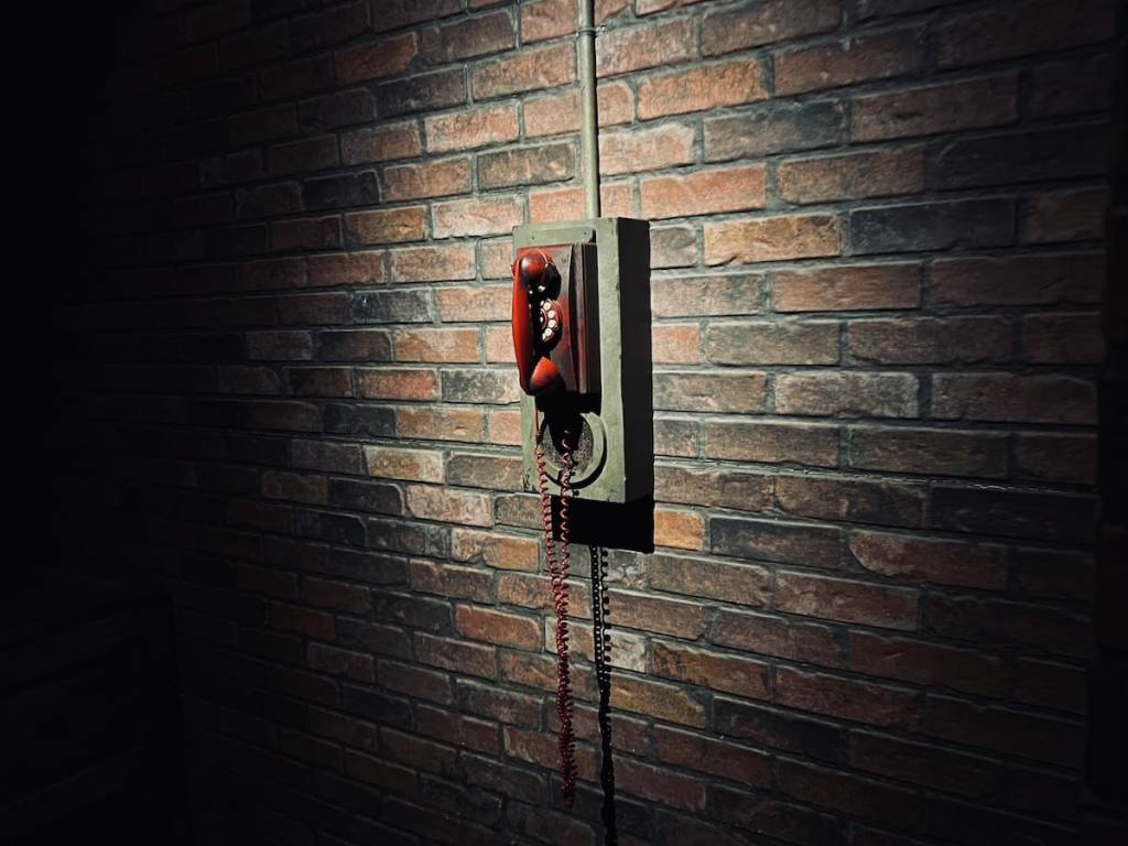 A spotlit red telephone hung on a brick wall.