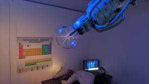 A large laser in a science lab. A body is laying on a desk.