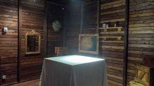 An attic, in the middle is a box covered in a white sheet and spot lit.