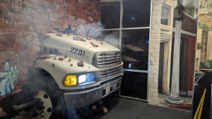 The front end of a truck protruding through a heavily damaged brick wall.