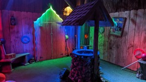 A well in a fenced in area lit in colorful light and surrounded by assorted objects as well as large lollypops.