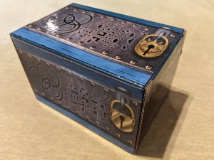 Closeup of an intricately decorated blue and grey cardboard puzzle box with images of gold locks on it.