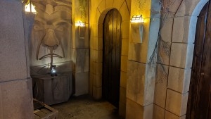 A stone temple with a carved face illuminated by sconces.