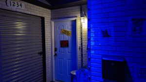 A front door beside a garage, the door has warning signs. The garage door and exterior walls have strange writing on them.