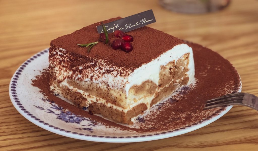 A large piece of tiramisu cake with a few pomegranate seeds atop.