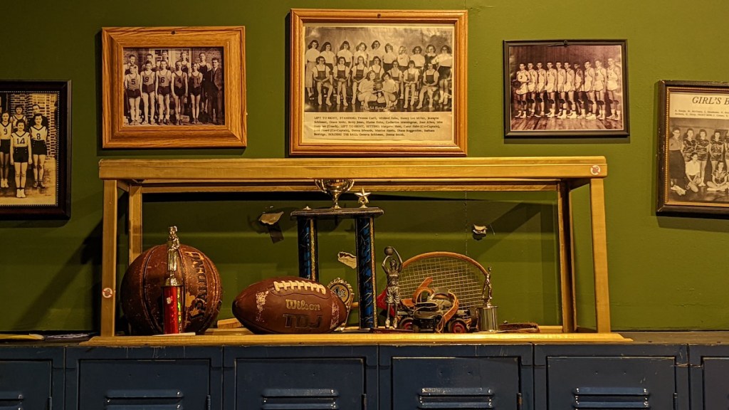 A trophy case in an old high school. There are team photos hung behind it.