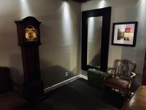 A grandfather clock beside a mirror and a chair.