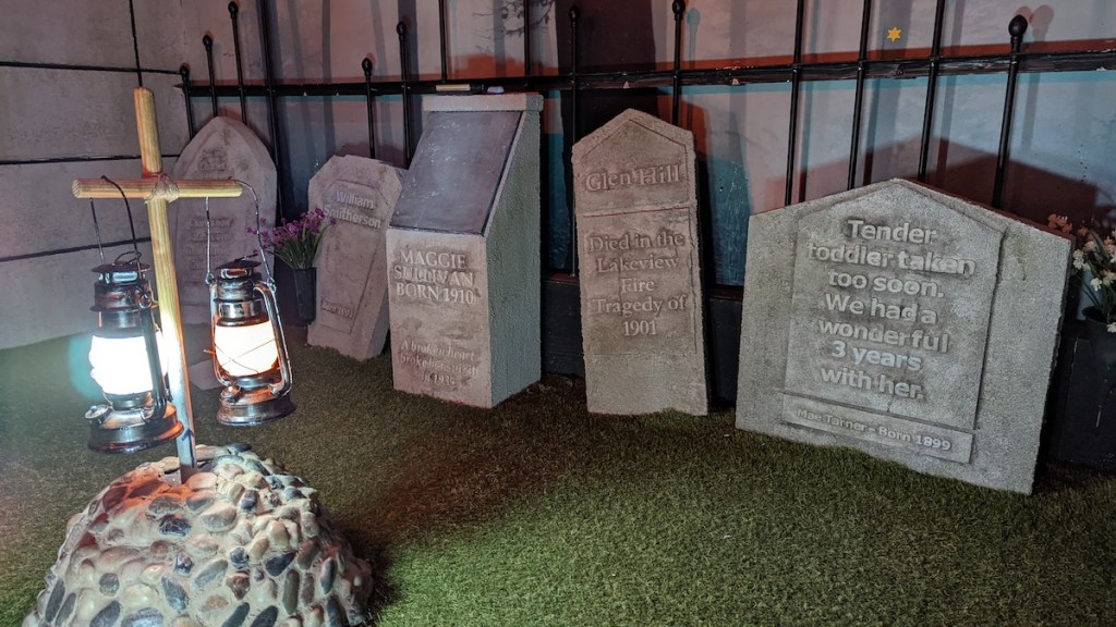 A cemetery filled with headstones and lit by two hanging lanterns.