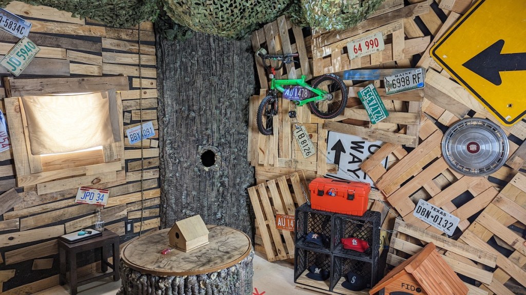 A wooden treehouse made from materials cobbled together including a bike, license plates, road signs, and hub caps.