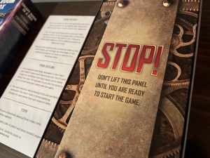 Close up, a panel atop the game box reads, "Stop! Don't lift this panel until you are ready to start the game."