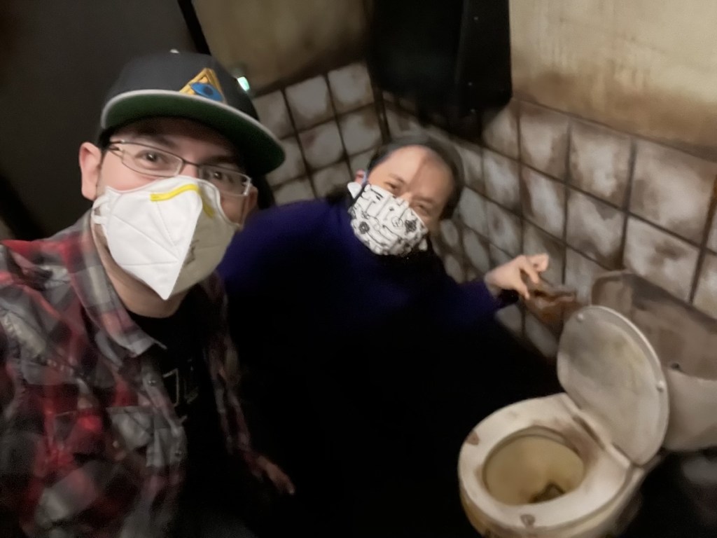 David & Tammy smiling for the camera while holding a turd over a toilet in an escape room.