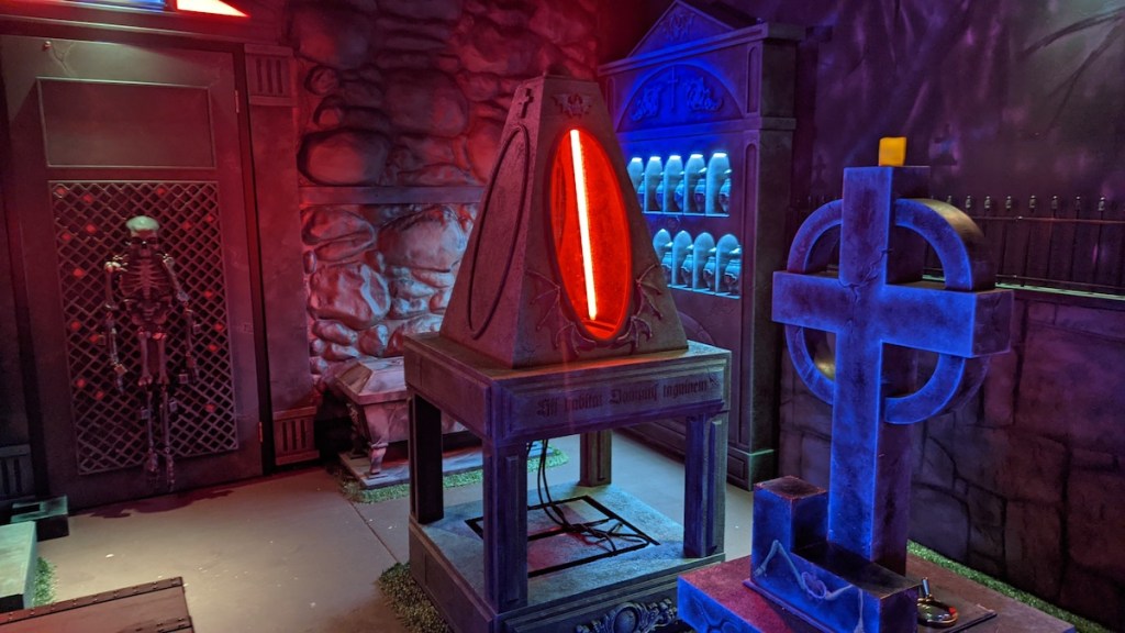 An unusual environment that looks like a cemetary crossed with a mad science lab. A skeleton, a crossed headstone, and a glowing pyramid can be viewed.