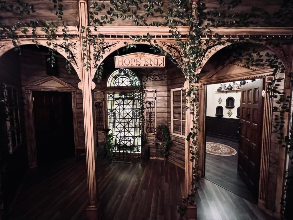 Entrance to Hope End has beautiful wood work covered in ivy, a stained glass window separates a door to a light room and a door to a dark room.