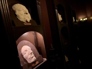 A wall of plaster death masks in a dark room.