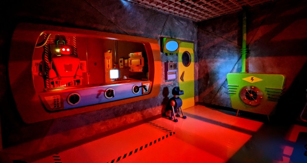 A robotic lab with a large red robot, a small robot dog, and a number of other equipment that looks like it could be from the Jetsons.