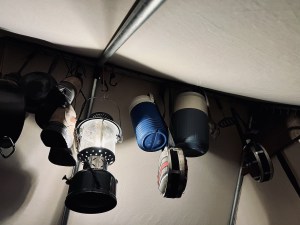View upward in a tent, camping equipment hangs from the tent's frame.