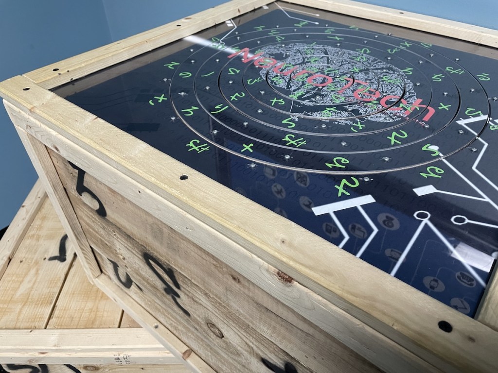 A crate with symbols painted on the side. Atop is a rotating disk puzzle with assorted symbols .